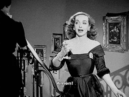 Movie gif. Bette Davis as Margo in All About Eve raising a glass and saying, "amen."