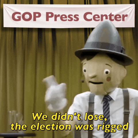 Video gif. Wooden Pinocchio puppet holds a hand on his hip and shakes his finger as his nose grows, saying, “We didn’t lose, the election was rigged. Above him, a banner reads, “GOP Press Center.”