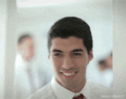 Video gif. Luis Suarez gives a friendly nod then smiles and points his fingers.
