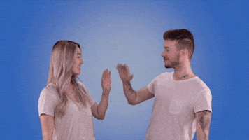 Video gif. A man and a woman in front of a blue backdrop smile at each other and high five, then turn and smile atus. The text, “teamwork!” appears above them when they high five.