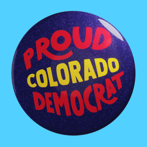 Text gif. A glossy blue pin has red and yellow text that reads, "Proud Colorado Democrat."