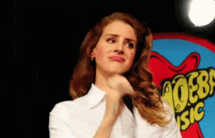 Celebrity gif. Lana Del Rey stands on stage with a microphone in her hand. She looks out at the crowd and pouts her lip exaggeratingly, batting her eyelashes like she’s a sad little girl. Her pout then changes into a smile.