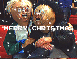 Video gif. Two men wearing creepy paper mache heads are sitting on the floor and hugging as they wave at us. It is snowing and the text reads, "Merry Christmas."