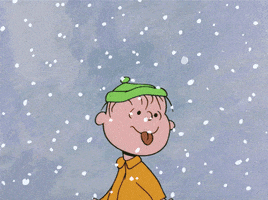 Cartoon gif. Charlie Brown stands in a flurry of snow and sticks out his tongue to catch a flake. 