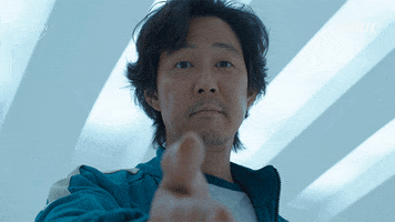 TV gif. Lee Jung Jae as Gi-hun in Squid Game reaches out his hand and offers a friendly smile. Text, "Wanna do this together?"
