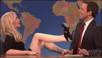 SNL gif. Kristen Wiig, dressed as a flirtatious character, legs wide above her head, uses a wheeled office chair to shuffle her hips into Seth Meyers' personal space, who cringes and covers his smile with embarrassment and discomfort.