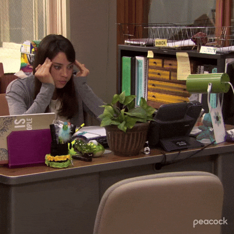 TV gif. Aubrey Plaza as April on Parks and Recreation sits at her office desk. The camera zooms in on her as she leans on her desk with her hands on her temples. Her expression is wide eyed and super stressed. 