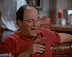 Seinfeld gif. Jason Alexander as George winks and points his finger across the table.