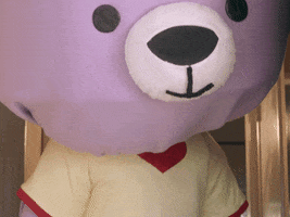 Video gif. Lilac-colored teddy bear mascot, with a big head and small body, turns his body toward us. The word "Hi!" pops up.