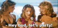 Movie gif. Sean Penn as Jeff Spicoli in Fast Times At Ridgemont High has sunblock on his nose and a lei around his neck while he holds a surfing trophy in his hands. Two beautiful women in bikinis stand next to him. A man holds a mic out to Jeff and he says, “Hey bud, let’s party!”