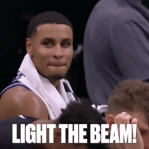 Sports gif. Keegan Murray of the Sacramento Kings has a towel around his shoulders and smirks as he sits on the bench and takes a sip from his water bottle. Text, "Light the beam!"