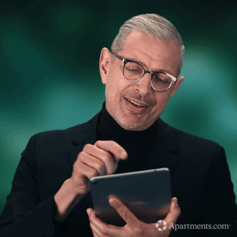 Celebrity gif. Jeff Goldblum gives a light, airy smile, bobbing his head from side to side as he scrolls an iPad.