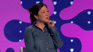 Reality TV gif. Margaret Cho on The Celebrity Dating Game. She's sitting in a chair pondering with her hand on her chin before coming to a realization and saying, "Oh," and looking at us suddenly.