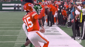 Sports gif. Patrick Mahomes of the Kansas City Chiefs stands on the field during a game, holding his arms out and balancing a football in one hand like he's playing to the crowd. 