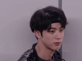 Celebrity gif. Jin from BTS hears something exciting and his face is totally shocked and he begins bouncing around eagerly.