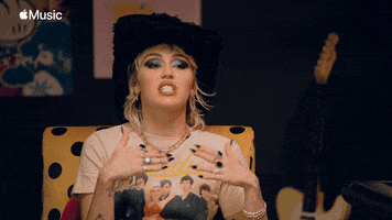 Celebrity gif. Wearing a furry cowboy hat and a Blondie T-shirt, Miley Cyrus sits in an Apple Music interview, speaking while gesturing "stop," slicing the air horizontally with her hands.