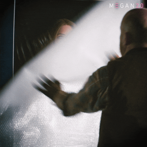 Sponsored gif. Man rips down a drop cloth and reveals the haunted doll Megan in her cardboard box. Text reads, “Surprise.”