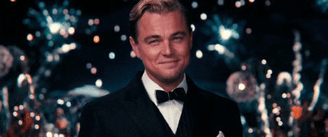 Leonardo DiCaprio z filmu Velký Gatsby, připíjející šampaňským s ohňostroji v pozadí.