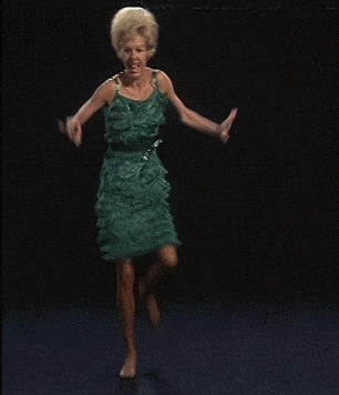 Video gif. A barefoot woman wearing a formal dress dances in celebration.