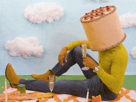 Video gif. Man wearing a birthday cake on his head toasts us with a wine glass. Text, "Here's to you."