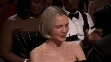 Oscars 2024 GIF. Grateful, Cary Mulligan scrunches up her face and puts a hand to her heart while the crowd applauds her. 