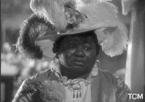 Movie gif. Black and white gif of Hattie McDaniel as Queenie in "Show Boat," wearing a big feather hat and a high-necked ruffled top, blinking and then bringing a gloved finger to her eye to dab away tears.