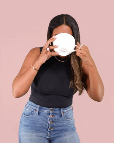 Video gif. Kamie Crawford drinks from a large tea cup that covers her whole face, lowering it to look at us skeptically before looking off screen.
