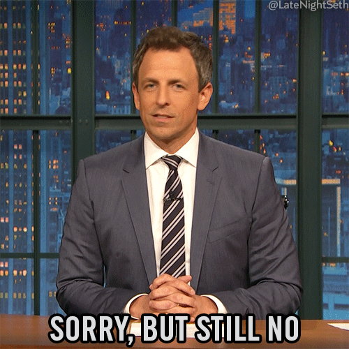 Late Night gif. Seth Meyers sits at his desk with his hands folded and he shakes his head back and forth vehemently while smirking. Text, "Sorry, but still no."