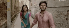 Movie gif. Kartik Aaryan as Vinod Shukla runs down an alley, holding hands with Kriti Sanon as Rashmi Trivedi in Luka Chuppi.