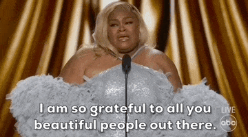 Oscars 2024 gif. Da'Vine Joy Randolph dazzles in a shimmering silver-blue dress with frilly, pom pom-like sleeves. Emotional, she tearfully addresses the audience and says, "I am so grateful to all you beautiful people out there."