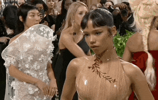 Met Gala 2024 gif. Taylor Russell wearing a custom Loewe freshly cut wood bodice embellished with burnt wood floral vines, poses for the cameras expertly, adjusts turning her back to the camera and looking over her shoulder.