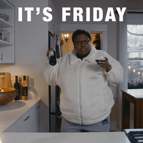 Video gif. A woman dances in her kitchen with a bottle of wine in one hand and a glass in the other. Text, "It's Friday!"