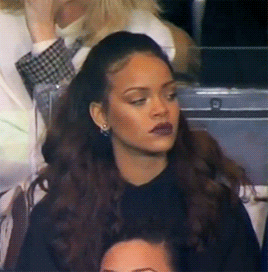 Celebrity gif. Musician Rihanna rolls her eyes and looks away in annoyance while seated in a crowd. 