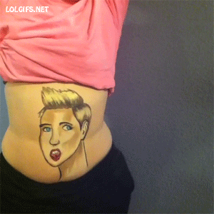 Video gif. Woman lifts her shirt, revealing a drawing of Miley Cyrus on her belly. She wiggles her hips as a man’s belly decorated with an enormous wrecking ball enters from the right, smashing into the depiction of Miley Cyrus.