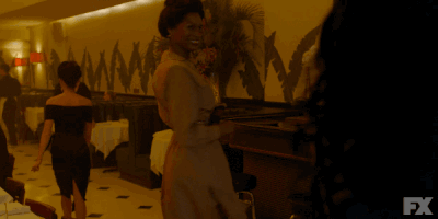 TV gif. Dominique Jackson as Elektra in Pose beams as she shimmies down in a squat before standing back up.
