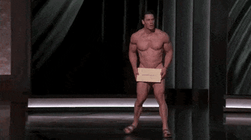 Oscars 2024 GIF. John Cena is in the middle of his nude journey to the microphone, still shuffling with the Oscar winner envelope covering his precious parts. He shuffles out horizontally, carefully taking small steps, trying to avoid any accidental peeks. His face is stressed. It's a long way to the microphone. 