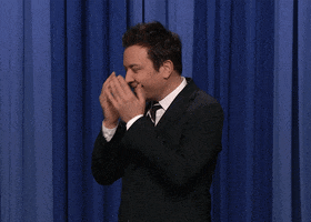 TV gif. Jimmy Fallon stands in front of a blue curtain, burying his face in his hands, then lowering his hands and shaking his head, looking down, embarrassed.