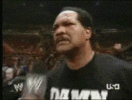 Sports gif. Wearing a black shirt that says “Damn,” WWE star Ron Simmons says into a microphone to a stadium full of people, “Damn!”