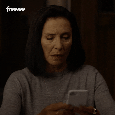 Video gif. A woman looks up from her phone, shaking her head, with a look of annoyance on her face.
