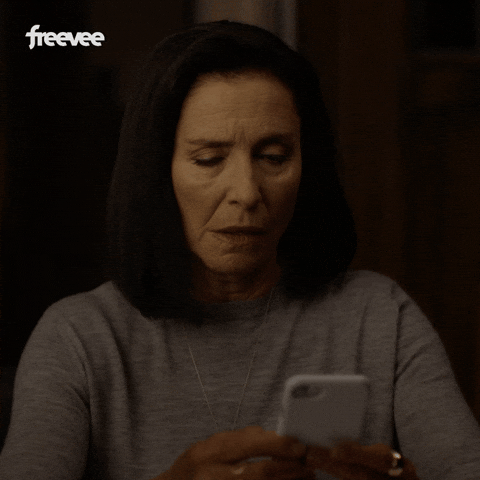 Video gif. A woman looks up from her phone, shaking her head, with a look of annoyance on her face.