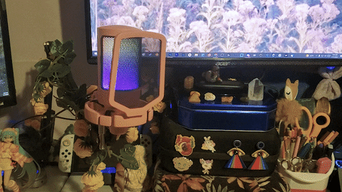 an animated image of the fifine microphone fully lit up with a cute, decorated desk setup behind it. the RGB lights are gently pulsating while heyshadylady's hand reaches from above and gently taps the top. upon contact with the microphone, the RGB lights shut off, and the mic is dark.