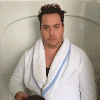 Video gif. Man stands in a shower in a white robe. He holds up a huge mug of coffee, larger than his head, and at first makes it seem like he’s going to drink from it, but instead he pours his right over his head.