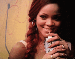Celebrity gif. Rihanna has the straw of a juice box in her mouth as she smiles and waves at us flirtatiously.