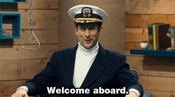 TV gif. Scott Aukerman on Comedy Bang Bang looks at us while wearing a boat captain’s hat. He waves his hand up and smirks as he says, “Welcome aboard.”