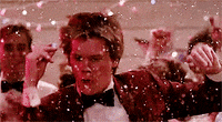 Movie gif. A party rages and confetti falls as Kevin Bacon as Ren in Footloose twirls, then shrugs confidently and straightens his bowtie. The crowd around him applauds.