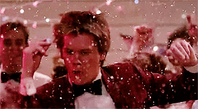 Sváteční gif s tancujícím mužem, obklopeného davem, na který padají třpytící se konfety.