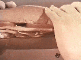 Video gif. From a retro sepia-toned 1960s film, a man and a woman share an enormous three-foot hoagie, each taking a bite from either end.