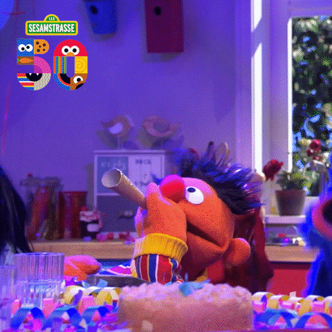 TV gif. The cast of Sesame Street are celebrating their 50th birthday, jumping and dancing joyfully as Ernie blows a gold glittery party horn from side to side. 