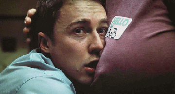 Movie gif. Edward Norton as The Narrator in Fight Club stares blankly as he rests his face on the chest of a person who strokes his hair. 