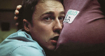 Movie gif. Edward Norton as The Narrator in Fight Club stares blankly as he rests his face on the chest of a person who strokes his hair. 